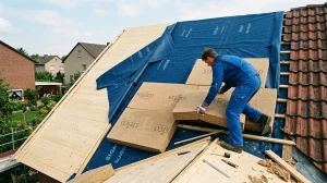 Handwerker verlegt Holzfaserplatten als Aufsparrendämmung auf Holzschalung und blauer Dampfbremse